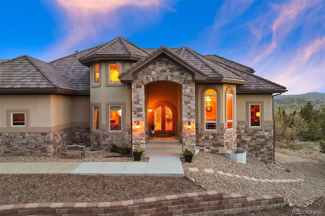 view of front of property with a tiled roof, french doors, stone siding, and stucco siding