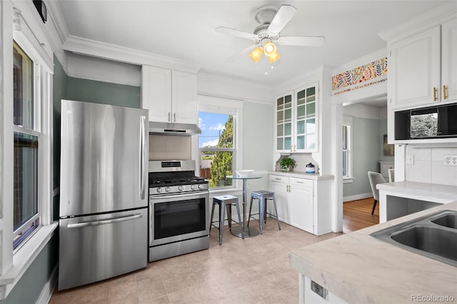 5008 Sherman St, Denver, CO 80216 - kitchen with stainless steel appliances, under cabinet range hood, white cabinets, backsplash, and ornamental molding
