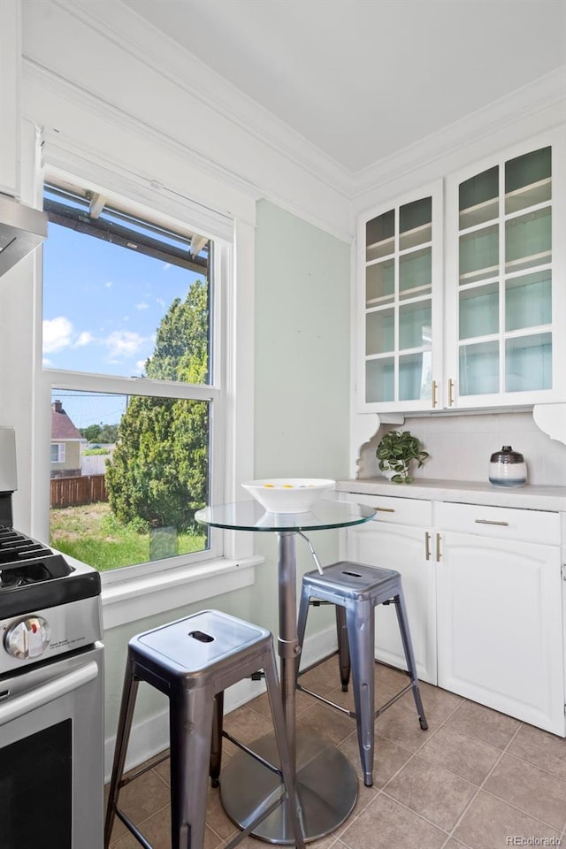 5008 Sherman St, Denver, CO 80216 - kitchen featuring stainless steel stove, glass insert cabinets, white cabinetry, ornamental molding, and light tile patterned floors