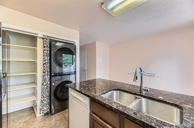 4130 E 94th Ave Unit B, Thornton, CO 80229 - kitchen featuring stacked washing machine and dryer, white dishwasher, dark stone countertops, light tile patterned floors, and a textured ceiling