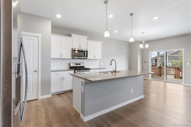 2248 Rosette Ln, Castle Rock, CO 80104 - kitchen featuring appliances with stainless steel finishes, a center island with sink, light wood-type flooring, tasteful backsplash, and a chandelier