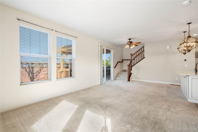 living room featuring ceiling fan with notable chandelier, stairway, light colored carpet, and baseboards