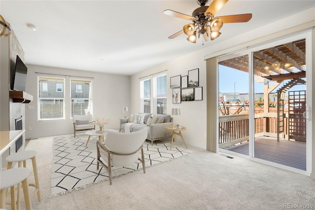 carpeted living room with visible vents, a ceiling fan, and a glass covered fireplace