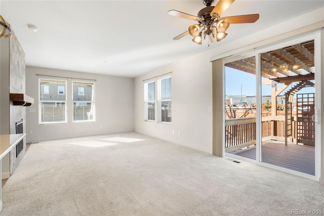 unfurnished living room with light carpet, a wealth of natural light, a fireplace, and ceiling fan