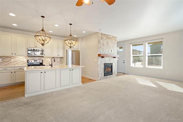 kitchen with a center island with sink, ceiling fan with notable chandelier, a fireplace, decorative light fixtures, and stainless steel appliances