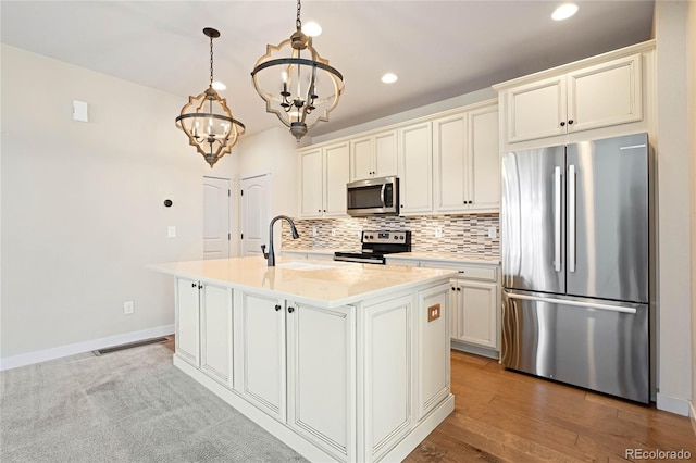 kitchen with an inviting chandelier, backsplash, pendant lighting, a center island with sink, and appliances with stainless steel finishes