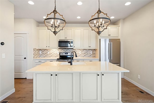 kitchen featuring pendant lighting, stainless steel appliances, an inviting chandelier, and a center island with sink