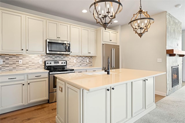 kitchen featuring a sink, appliances with stainless steel finishes, a tiled fireplace, a notable chandelier, and backsplash