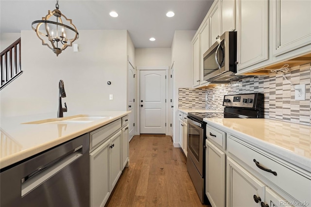 kitchen with light wood-type flooring, stainless steel appliances, sink, decorative light fixtures, and a notable chandelier