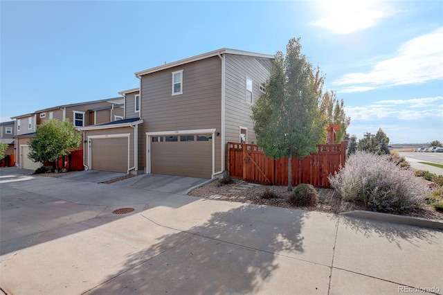 view of property exterior featuring concrete driveway, an attached garage, and fence