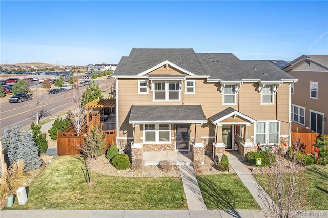 view of front of house with stone siding, a shingled roof, a front lawn, and fence