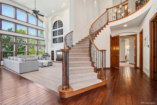 stairs featuring a towering ceiling, arched walkways, ceiling fan, hardwood / wood-style floors, and baseboards