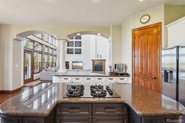 kitchen with stainless steel fridge with ice dispenser, gas cooktop, open floor plan, decorative columns, and arched walkways