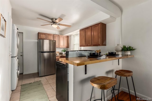 kitchen featuring a breakfast bar, wooden counters, stacked washing maching and dryer, and stainless steel refrigerator