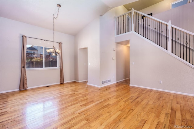 unfurnished living room with high vaulted ceiling, a chandelier, and light hardwood / wood-style flooring