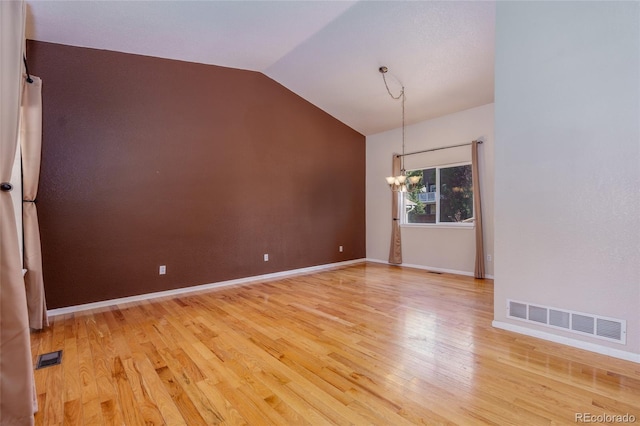 empty room featuring an inviting chandelier, hardwood / wood-style flooring, and vaulted ceiling