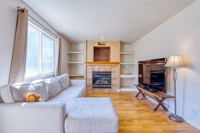 living room featuring built in features, light hardwood / wood-style flooring, and a tile fireplace