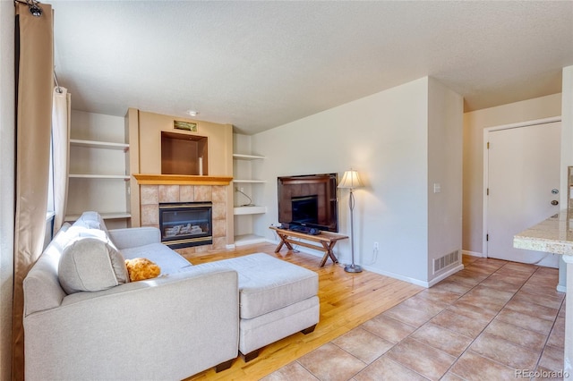 living room featuring a tiled fireplace, built in features, light hardwood / wood-style floors, and a textured ceiling