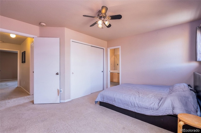 bedroom featuring a closet, light carpet, ensuite bathroom, and ceiling fan