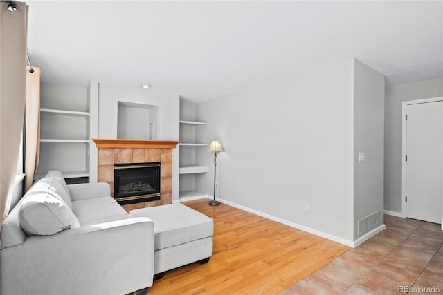 living room with built in shelves, visible vents, wood finished floors, a tile fireplace, and baseboards