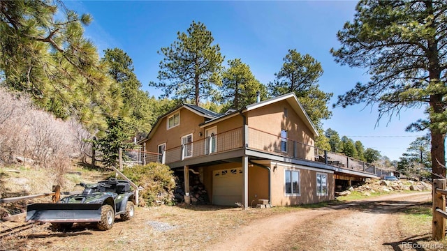 view of property exterior featuring a deck, an attached garage, driveway, and stucco siding