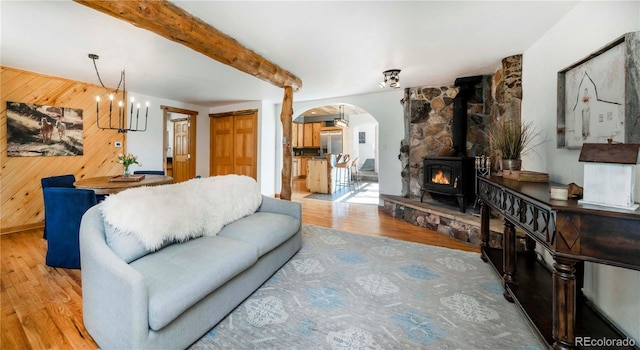 living room featuring an inviting chandelier, a wood stove, arched walkways, wood walls, and wood finished floors