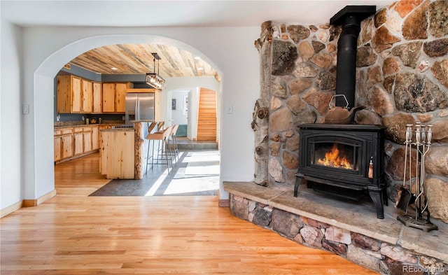 unfurnished living room featuring a wood stove, arched walkways, stairs, baseboards, and light wood-type flooring