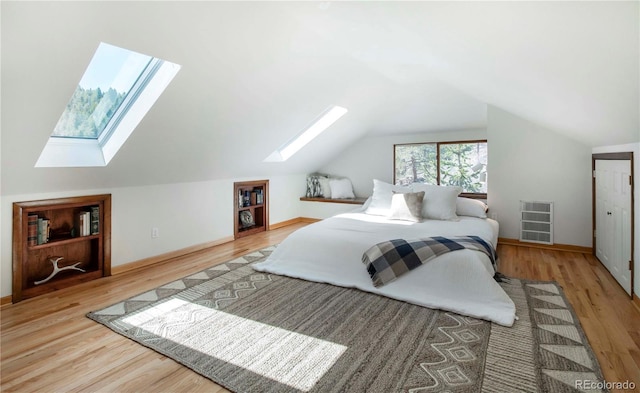 bedroom with vaulted ceiling with skylight, baseboards, and wood finished floors