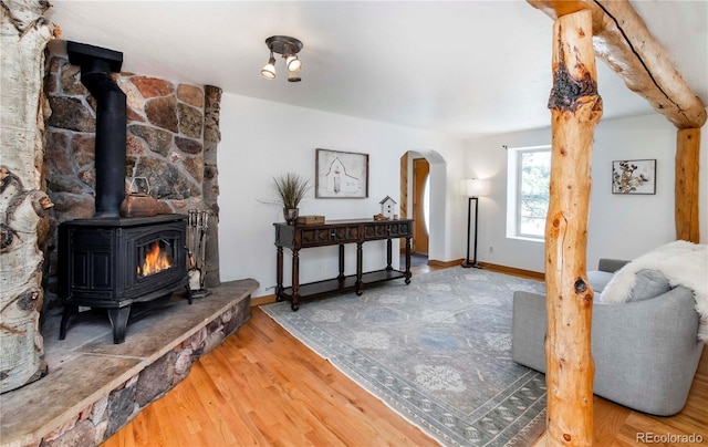 living area with arched walkways, baseboards, wood finished floors, and a wood stove