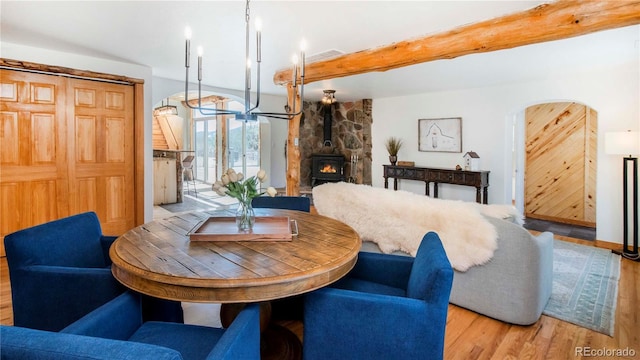 dining room featuring visible vents, arched walkways, a wood stove, wood finished floors, and beamed ceiling