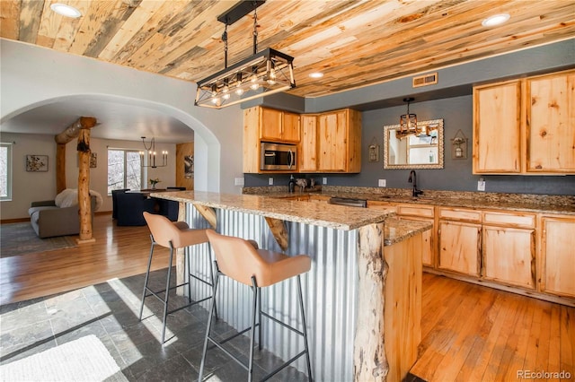 kitchen featuring wood ceiling, arched walkways, stainless steel microwave, a notable chandelier, and light brown cabinets