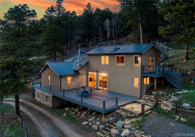 back of property at dusk featuring a standing seam roof, a wooden deck, stucco siding, and metal roof