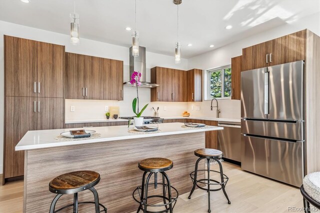 kitchen featuring decorative light fixtures, a center island, wall chimney range hood, appliances with stainless steel finishes, and a breakfast bar