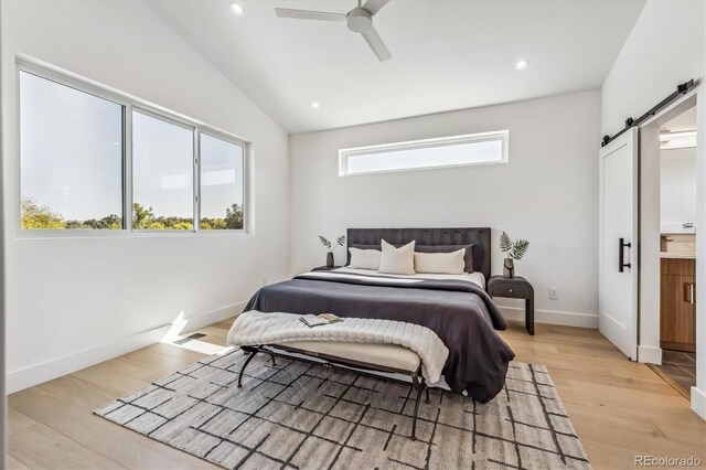 bedroom with ceiling fan, light hardwood / wood-style floors, ensuite bath, a barn door, and vaulted ceiling