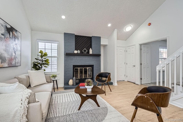 living room featuring a brick fireplace, a wealth of natural light, lofted ceiling, and light wood-type flooring