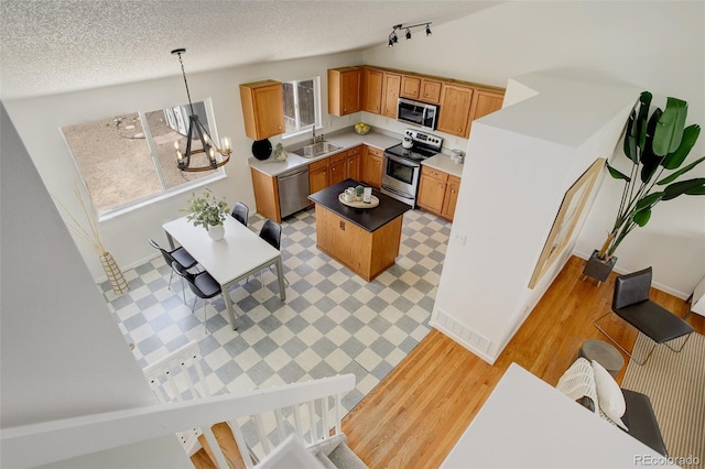 kitchen featuring a center island, a sink, light wood finished floors, decorative light fixtures, and appliances with stainless steel finishes