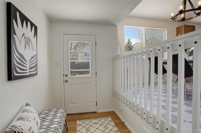 doorway to outside with a wealth of natural light, light wood finished floors, baseboards, and an inviting chandelier