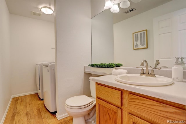 bathroom with independent washer and dryer, wood finished floors, visible vents, and toilet