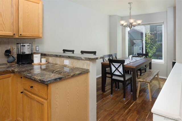 77 Spyglass Ln Unit 77, Silverthorne, CO 80498 - kitchen featuring a peninsula, dark wood-type flooring, a chandelier, dark stone counters, and hanging light fixtures