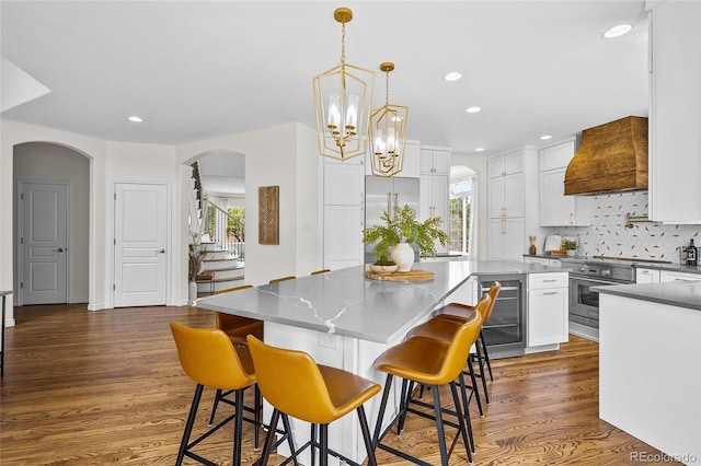 10802 W Indore Dr, Littleton, CO 80127 - kitchen featuring custom exhaust hood, arched walkways, backsplash, beverage cooler, and stainless steel stove