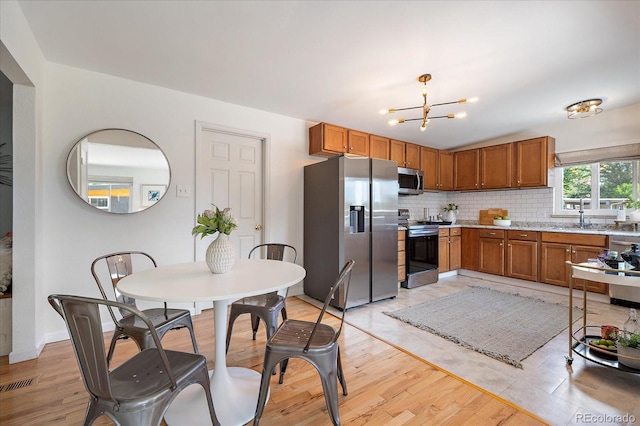 5975 Dover St, Arvada, CO 80004 - kitchen with stainless steel appliances, brown cabinetry, a chandelier, decorative backsplash, and light stone counters