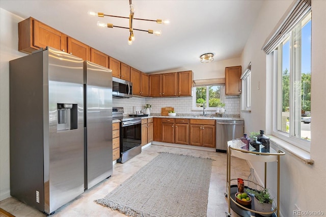 5975 Dover St, Arvada, CO 80004 - kitchen featuring stainless steel appliances, decorative backsplash, brown cabinets, a chandelier, and light stone counters