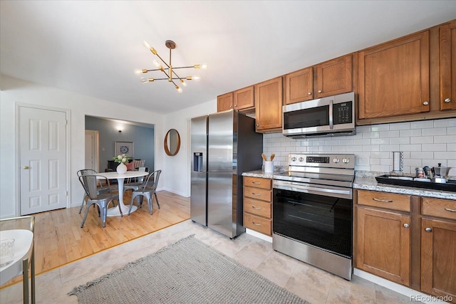 5975 Dover St, Arvada, CO 80004 - kitchen with appliances with stainless steel finishes, brown cabinetry, tasteful backsplash, and a chandelier