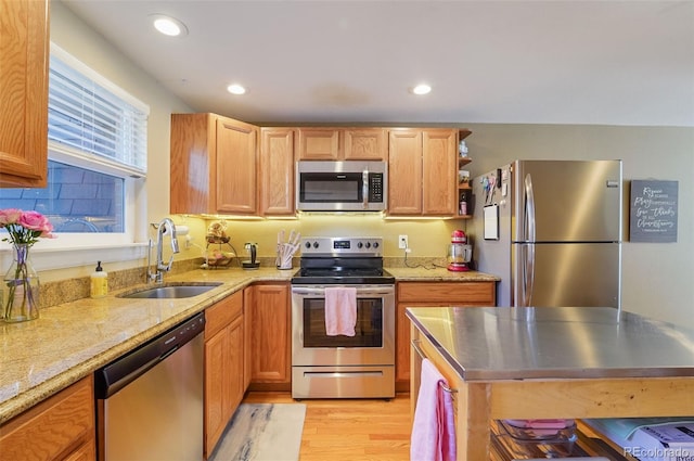 kitchen with light wood-type flooring, stainless steel appliances, light stone countertops, and a sink