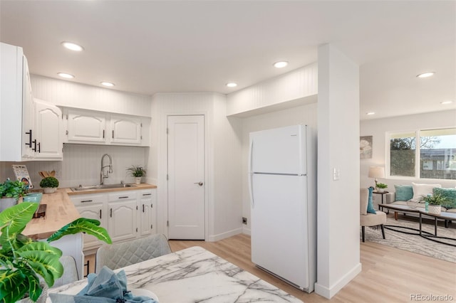 kitchen with backsplash, sink, white fridge, light hardwood / wood-style floors, and white cabinetry