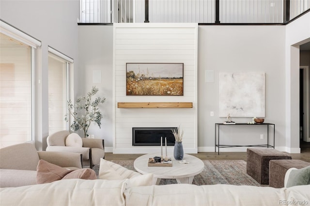 living room with a fireplace, a towering ceiling, and wood-type flooring