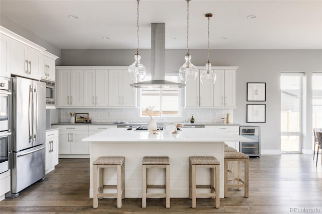 kitchen with wine cooler, island exhaust hood, decorative light fixtures, a center island with sink, and appliances with stainless steel finishes