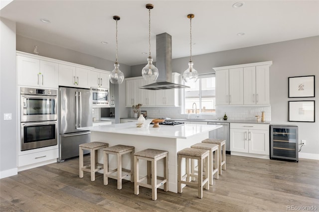 kitchen featuring wine cooler, appliances with stainless steel finishes, a kitchen island, white cabinetry, and island exhaust hood