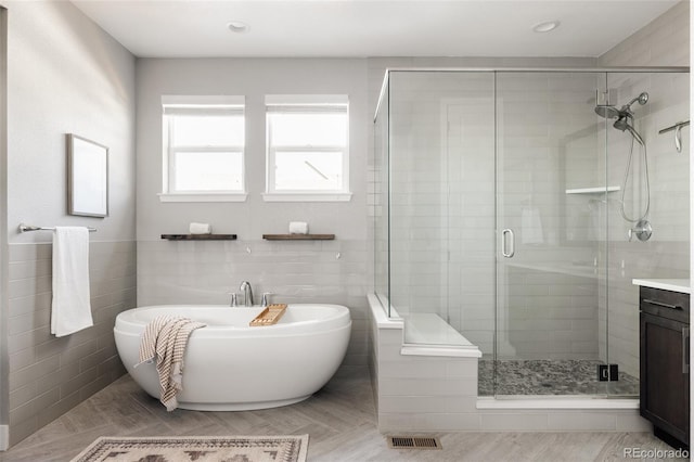 bathroom featuring separate shower and tub, vanity, and tile walls