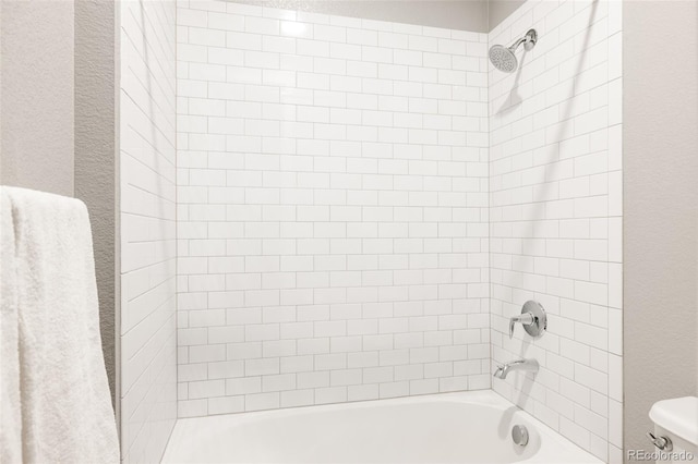 bathroom with toilet and tiled shower / bath